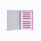 An open gray presentation box showing a pink interior tray with multiple rows of black false eyelashes arranged neatly.
